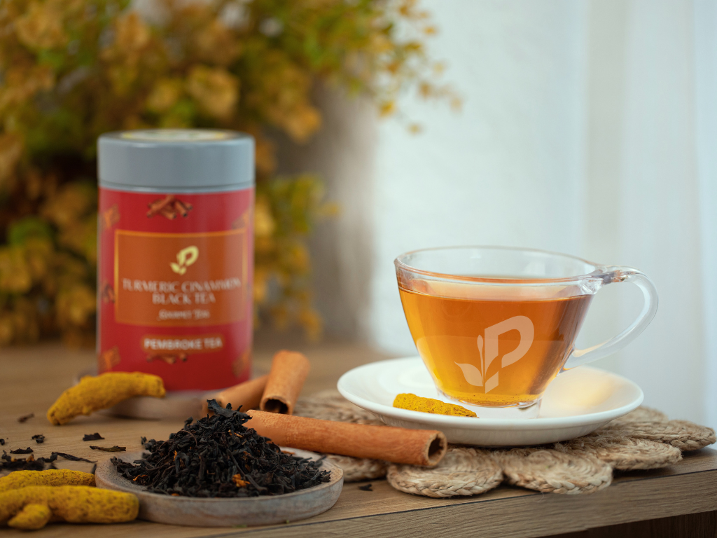 Tea cup with tea leaves, cinnamon sticks, and a canister on a wooden surface. - Turmeric Cinnamon Tea by Pembroke tea